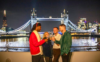 Guests enjoying a Christmas dinner party on a Thames River cruise with Tower Bridge in the background.