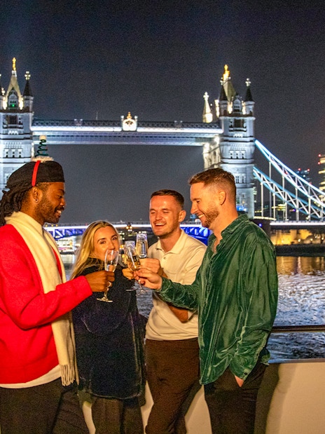 Guests enjoying a Christmas dinner party on a Thames River cruise with Tower Bridge in the background.