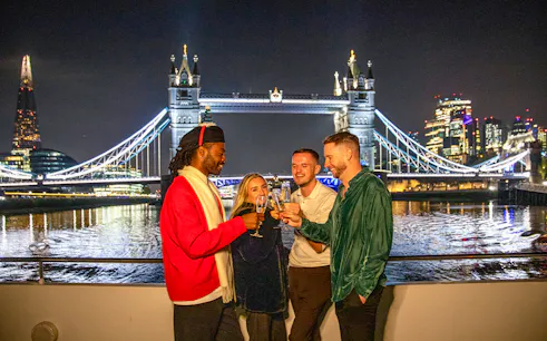 Guests enjoying a Christmas dinner party on a Thames River cruise with Tower Bridge in the background.