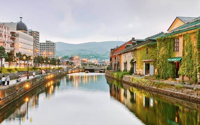 Otaru Canal at dusk with historic warehouses and city lights reflecting on the water.