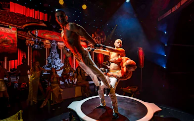 Acrobats performing on stage at Rouge show with Roman-themed backdrop.