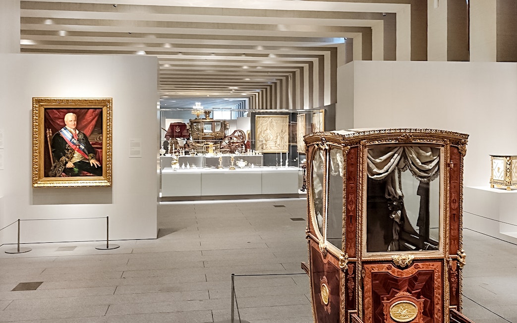 Royal Collections Gallery in Madrid featuring a historic carriage and portrait.