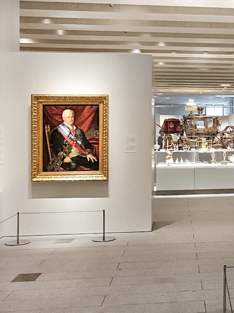 Royal Collections Gallery in Madrid featuring a historic carriage and portrait.
