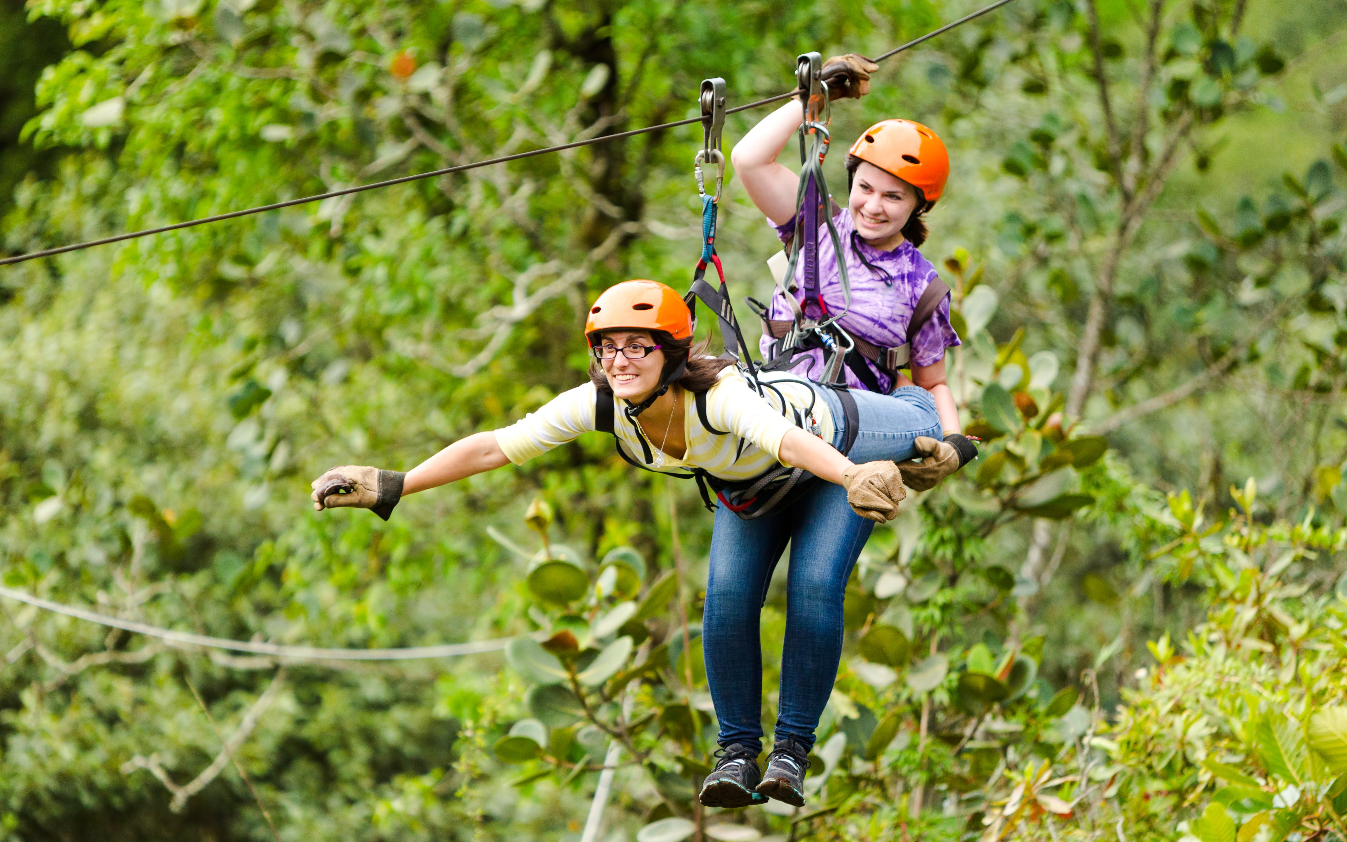 Woman zip-lining in tandem through lush forest.