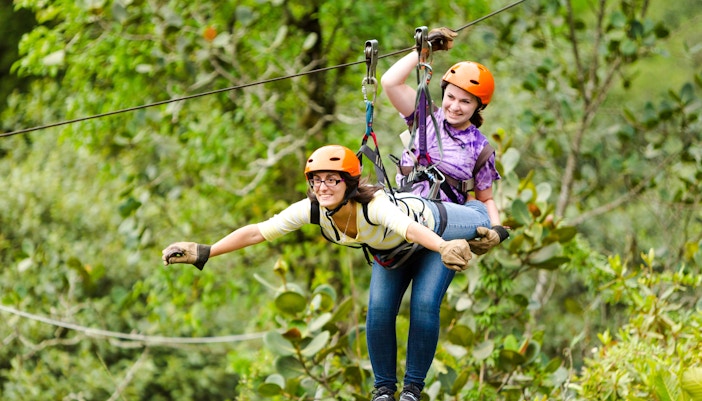 Woman zip-lining in tandem through lush forest.