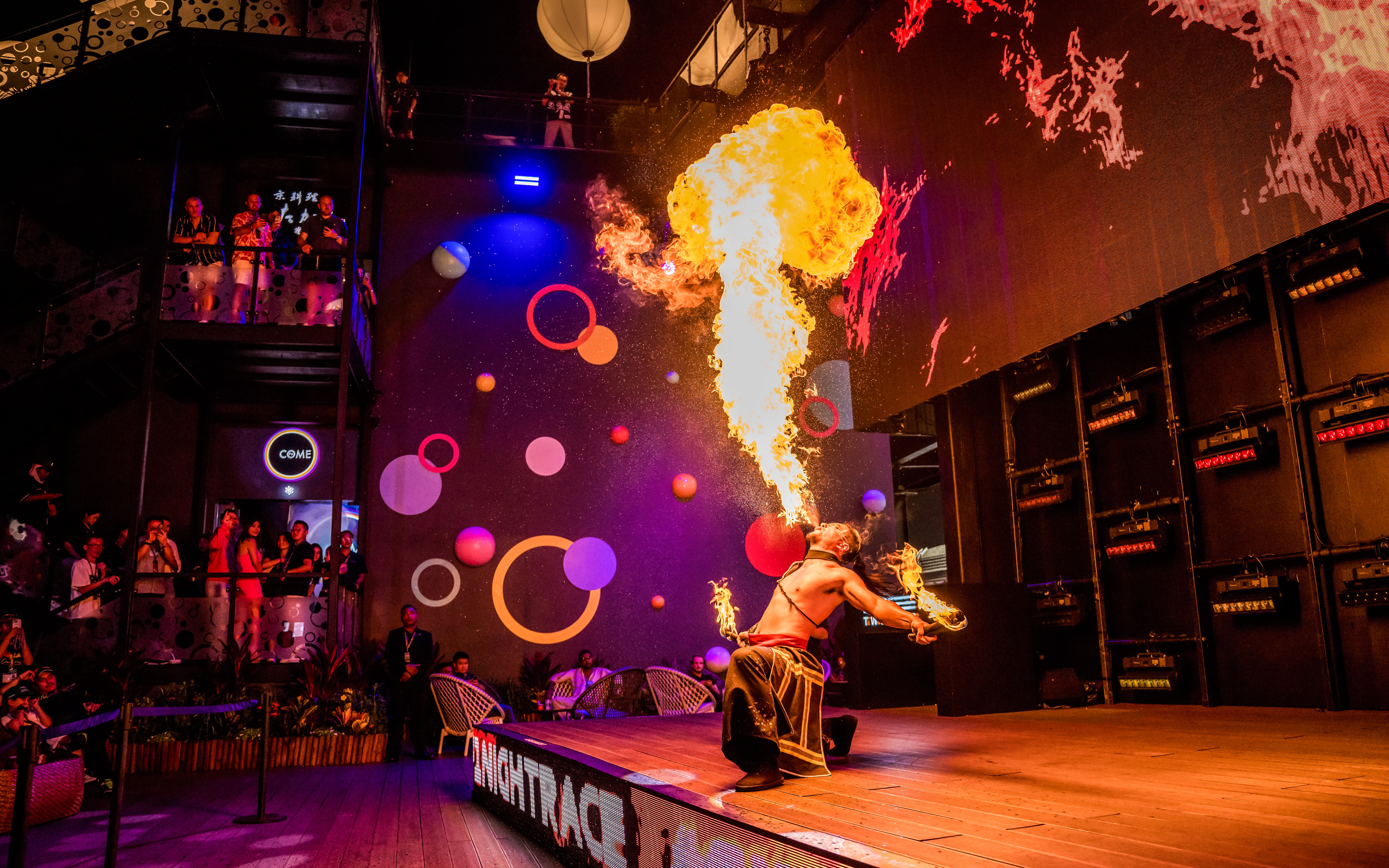 Fire performer entertaining audience with a dramatic flame display at a vibrant indoor venue.