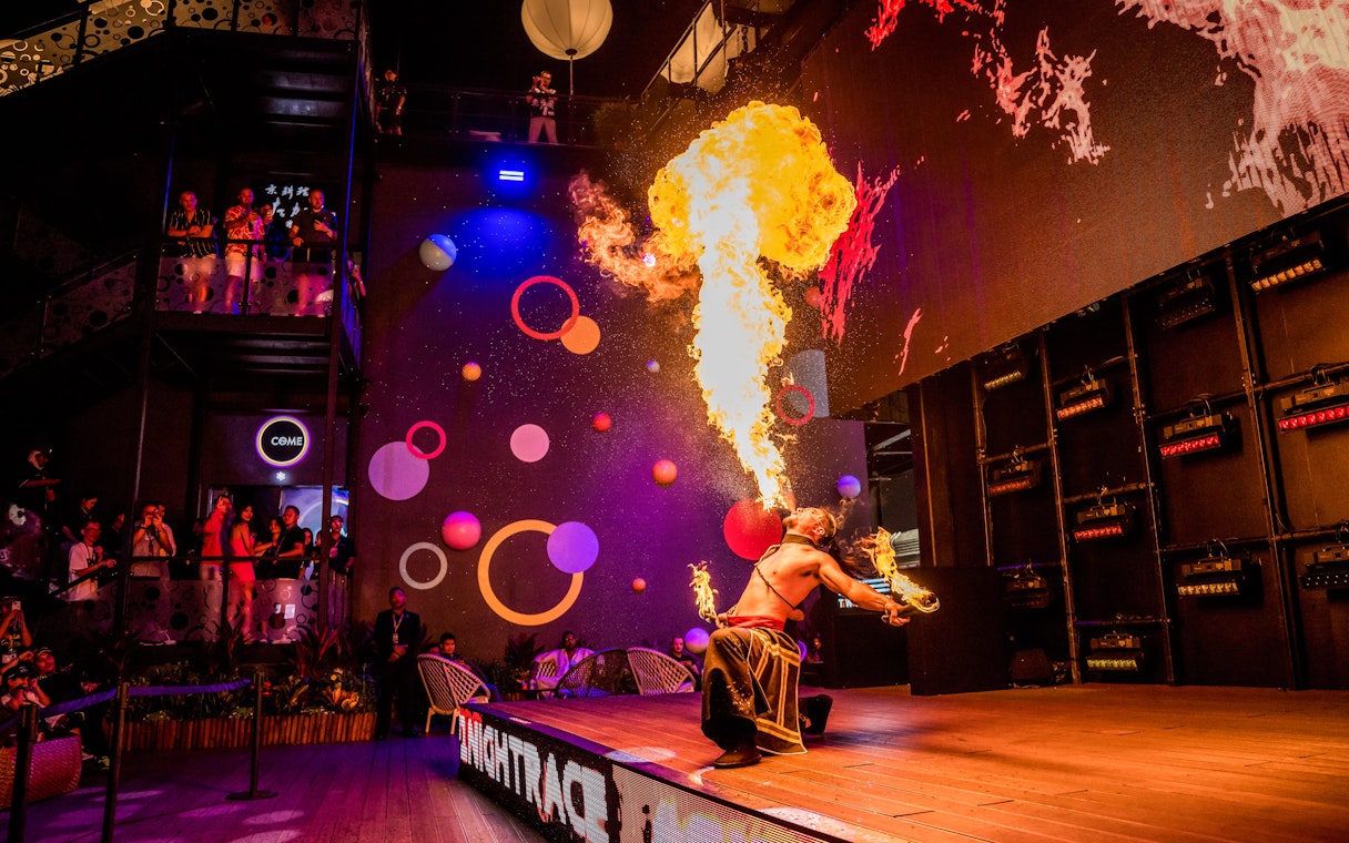Fire performer entertaining audience with a dramatic flame display at a vibrant indoor venue.