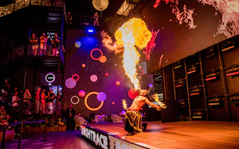 Fire performer entertaining audience with a dramatic flame display at a vibrant indoor venue.