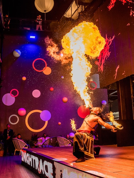 Fire performer entertaining audience with a dramatic flame display at a vibrant indoor venue.