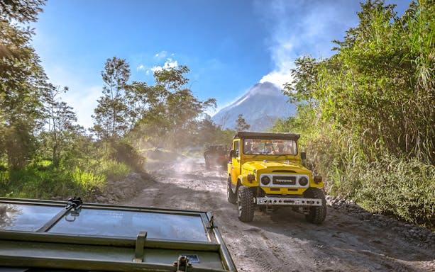 Off-road vehicles driving on a dirt path with a volcano in the background during a private day tour.