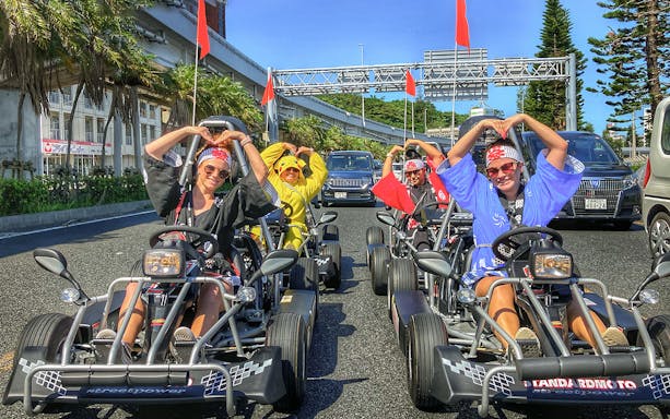 Go-karting group in costumes on Okinawa street with palm trees and traffic.