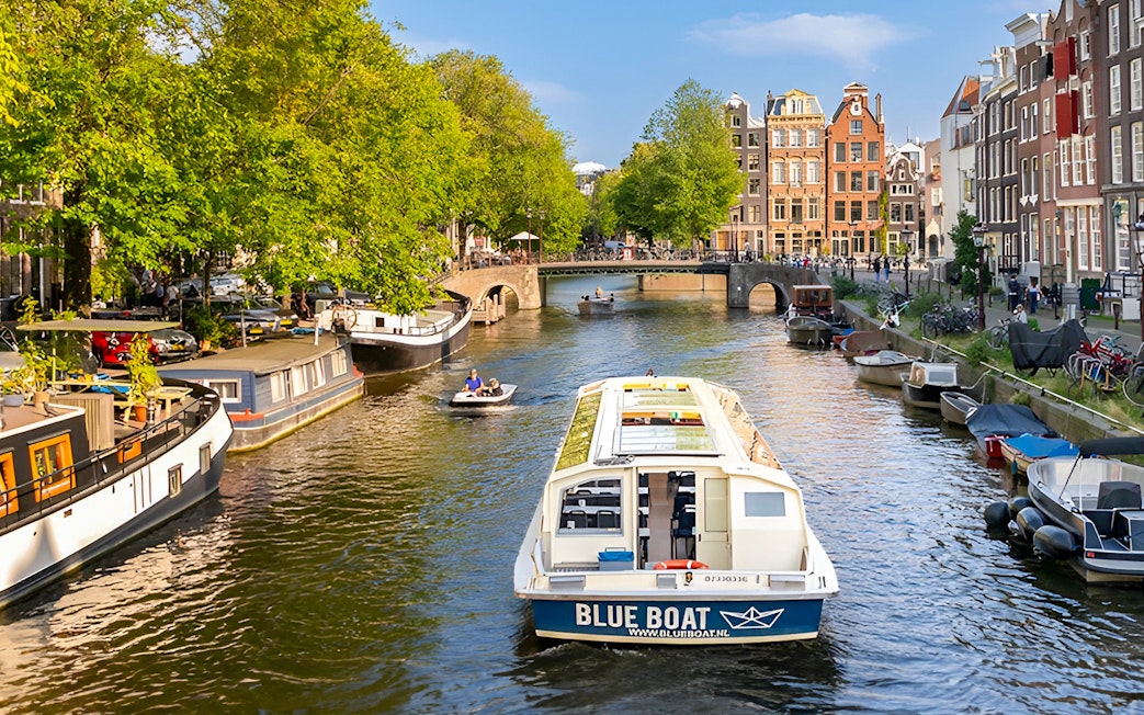Canal cruise boat on Amsterdam canal with historic buildings and bridge.