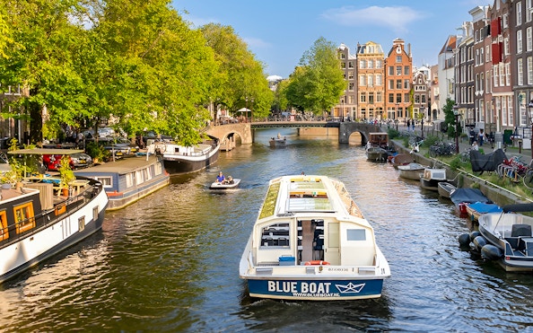 Canal cruise boat on Amsterdam canal with historic buildings and bridge.