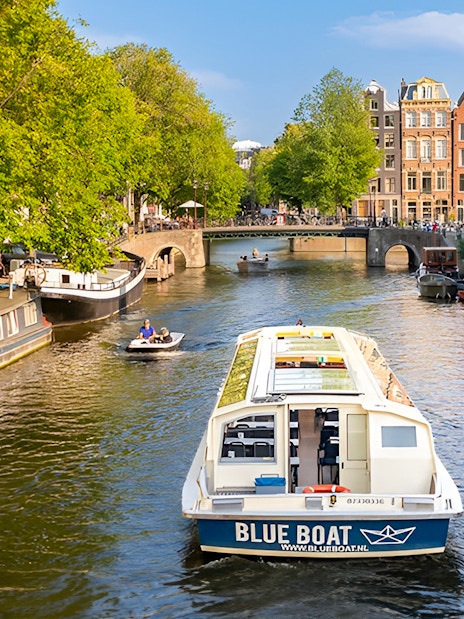 Canal cruise boat on Amsterdam canal with historic buildings and bridge.