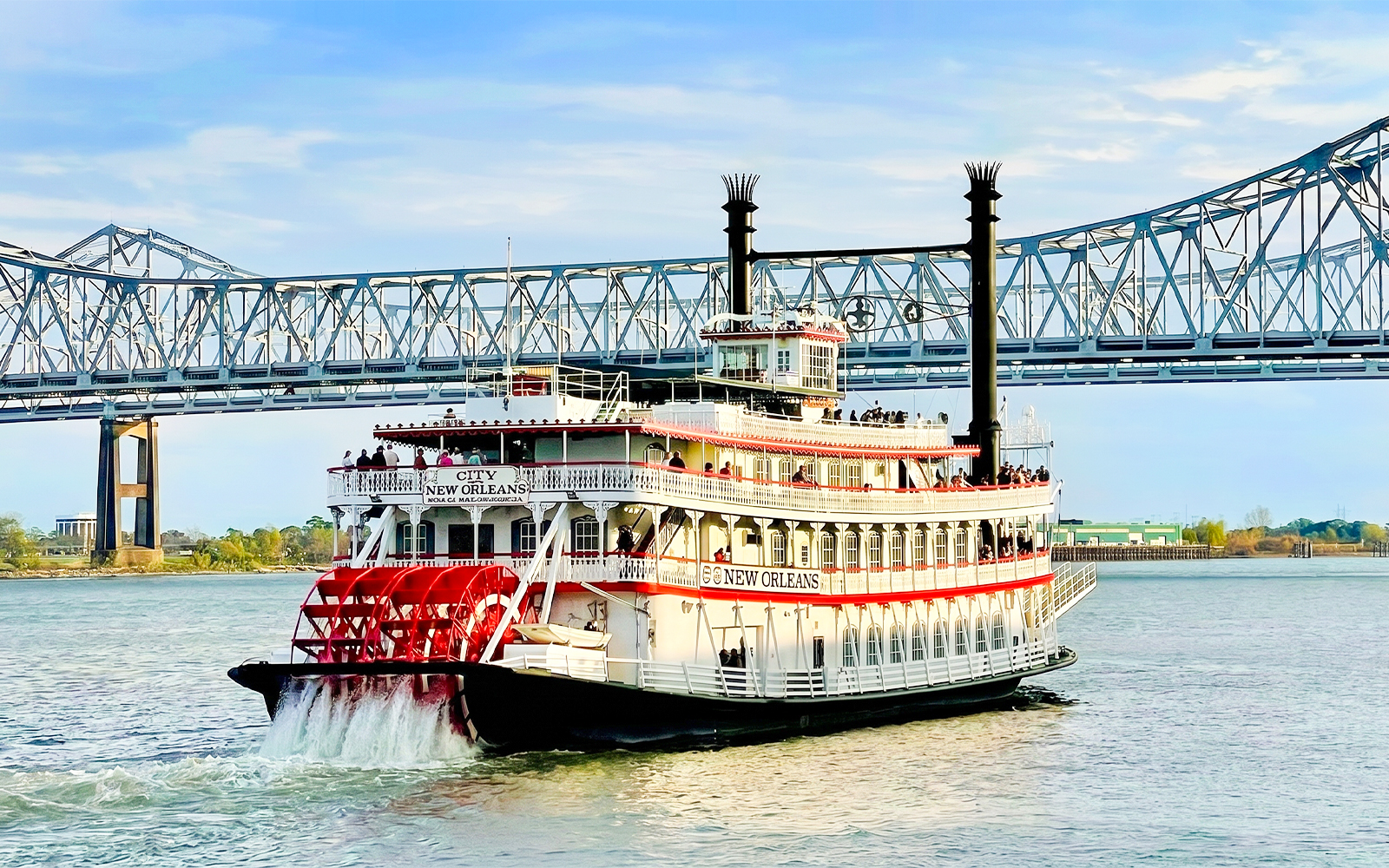 Riverboat cruising on the Mississippi River in New Orleans with a bridge in the background.