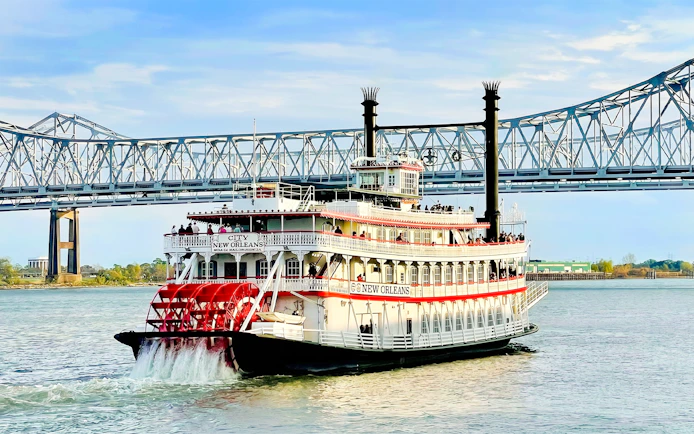 Riverboat cruising on the Mississippi River in New Orleans with a bridge in the background.