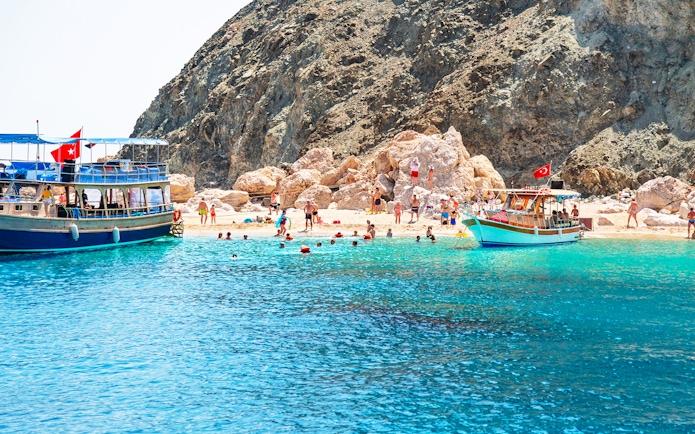 Boat trip to Suluada Island from Antalya with people swimming near rocky shore.