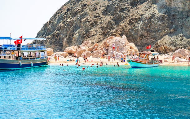 Boat trip to Suluada Island from Antalya with people swimming near rocky shore.