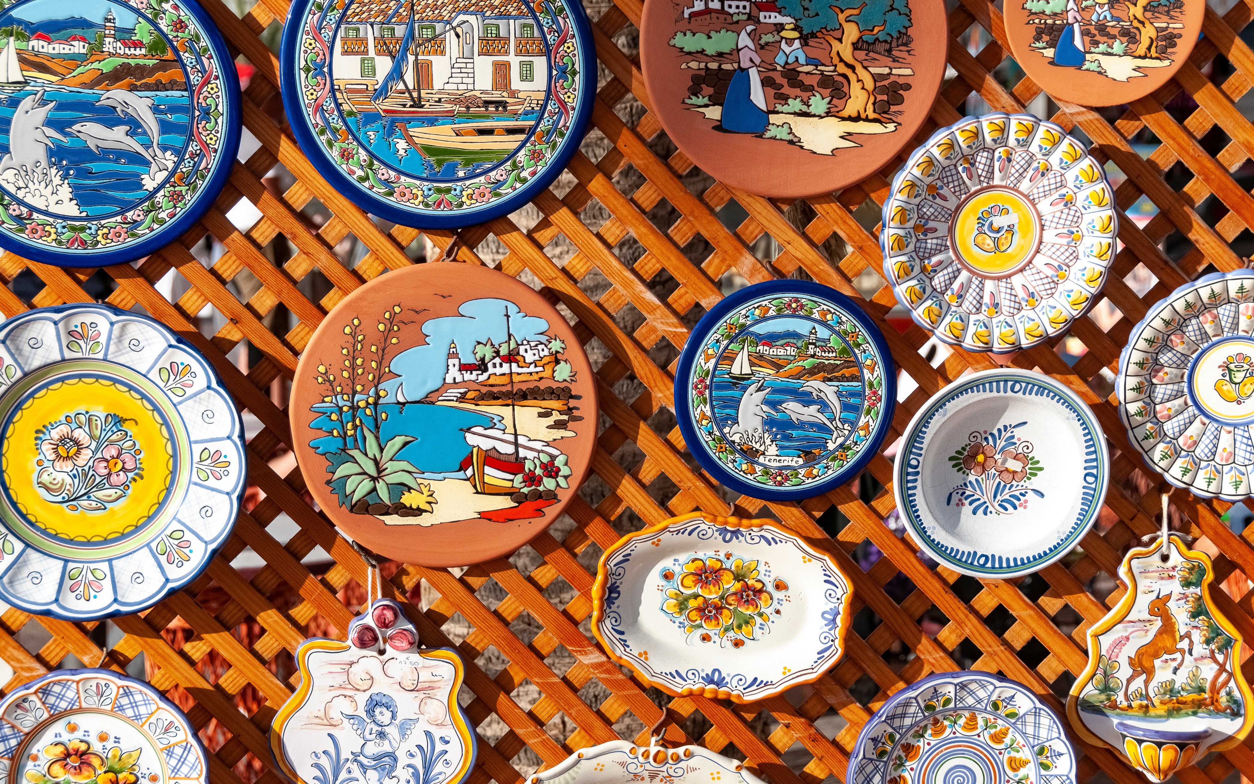 Ceramic plates with colorful Tenerife designs displayed on a wooden lattice.