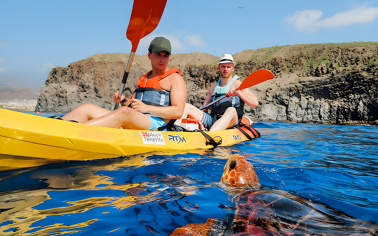 Tourists kayaking near a turtle in Tenerife island waters.