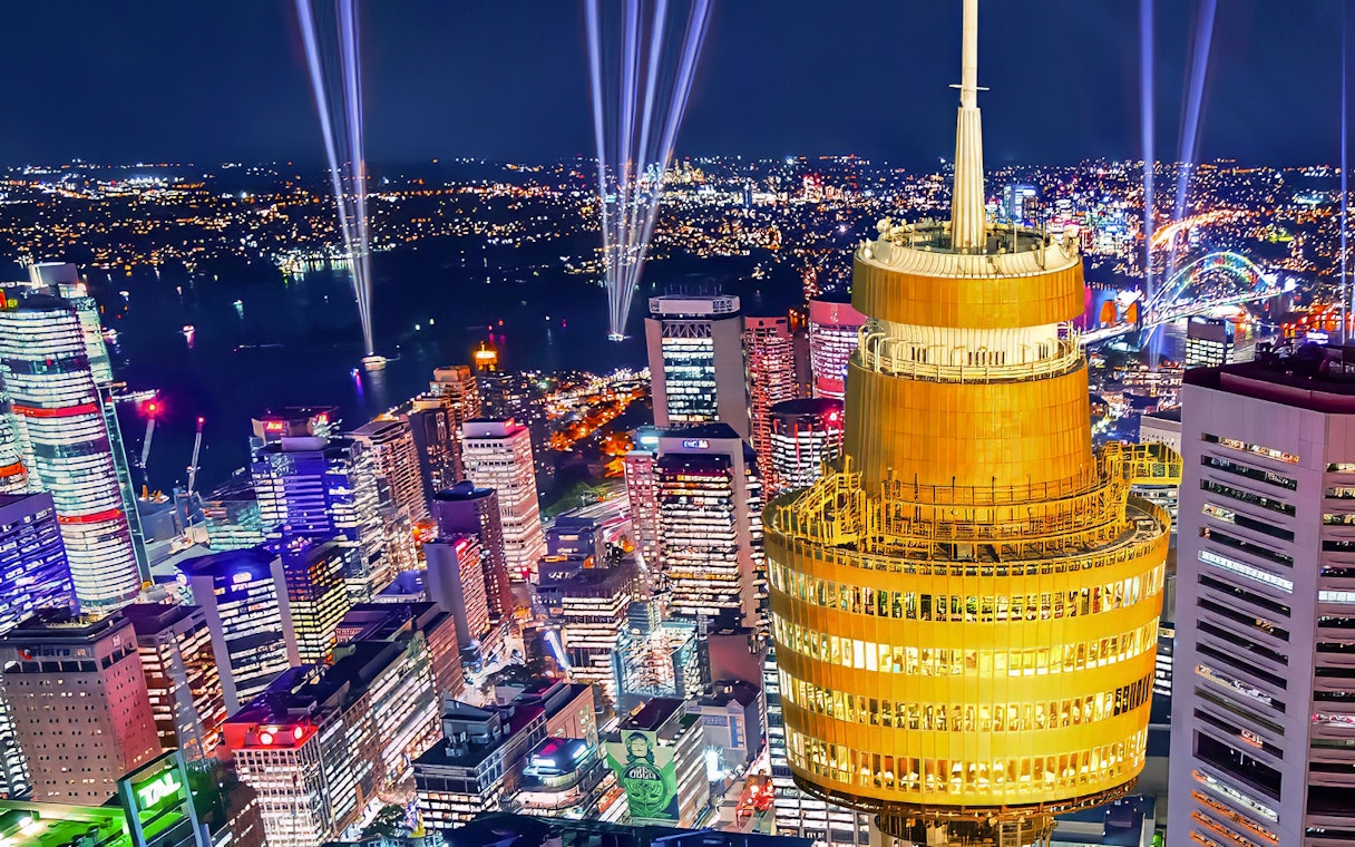 Sydney skyline at night featuring illuminated Sydney Tower and city lights.