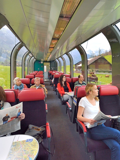Passengers enjoying scenic view from panoramic train window in Swiss countryside.