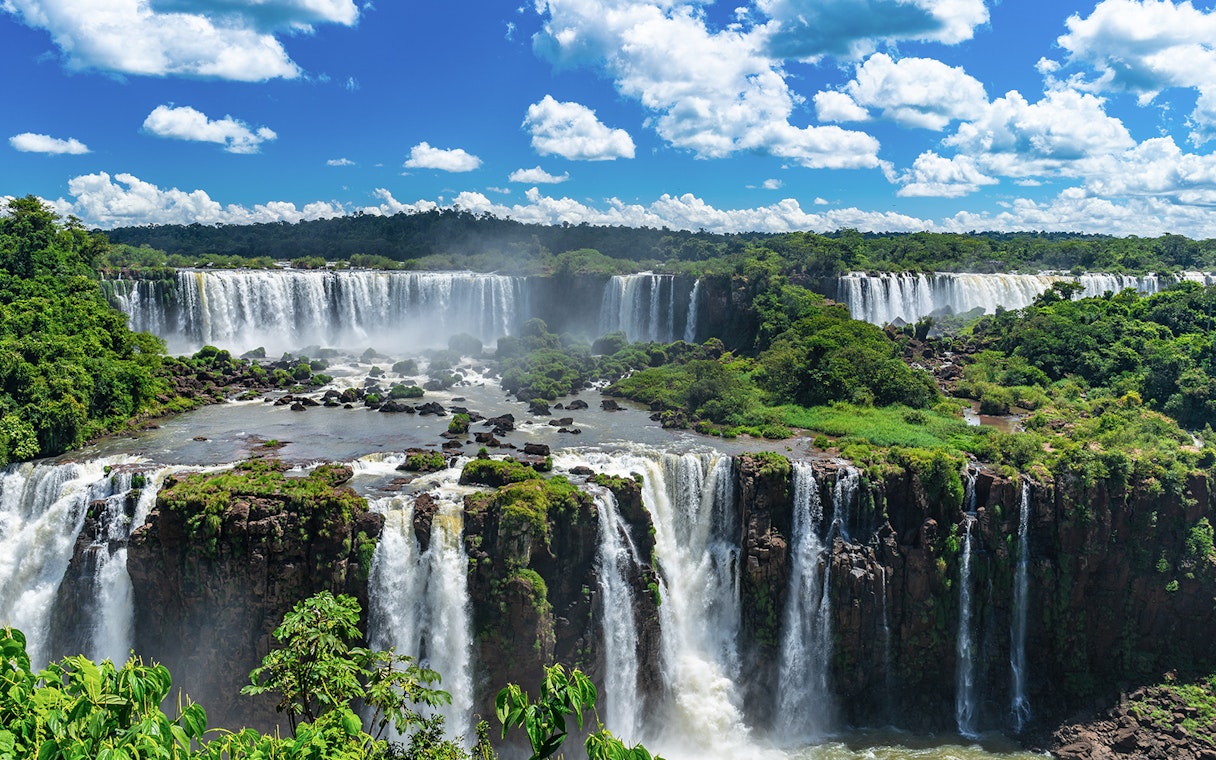 Iguazu Falls cascading over lush green cliffs under a blue sky.