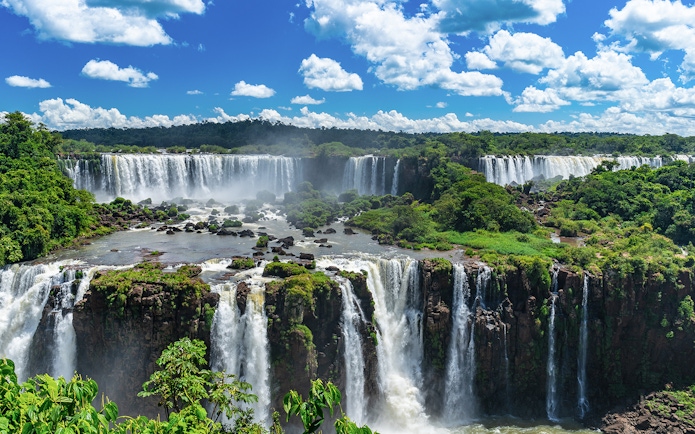 Iguazu Falls cascading over lush green cliffs under a blue sky.