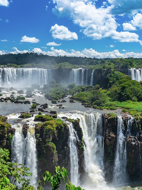 Iguazu Falls cascading over lush green cliffs under a blue sky.