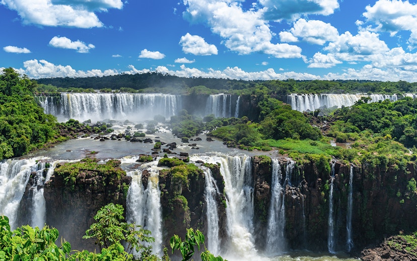 Iguazu Falls cascading over lush green cliffs under a blue sky.