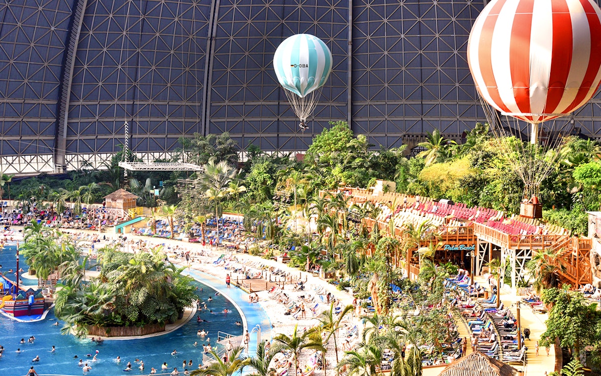 Tropical Islands Resort indoor beach with palm trees and hot air balloons.