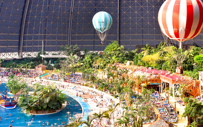 Tropical Islands Resort indoor beach with palm trees and hot air balloons.