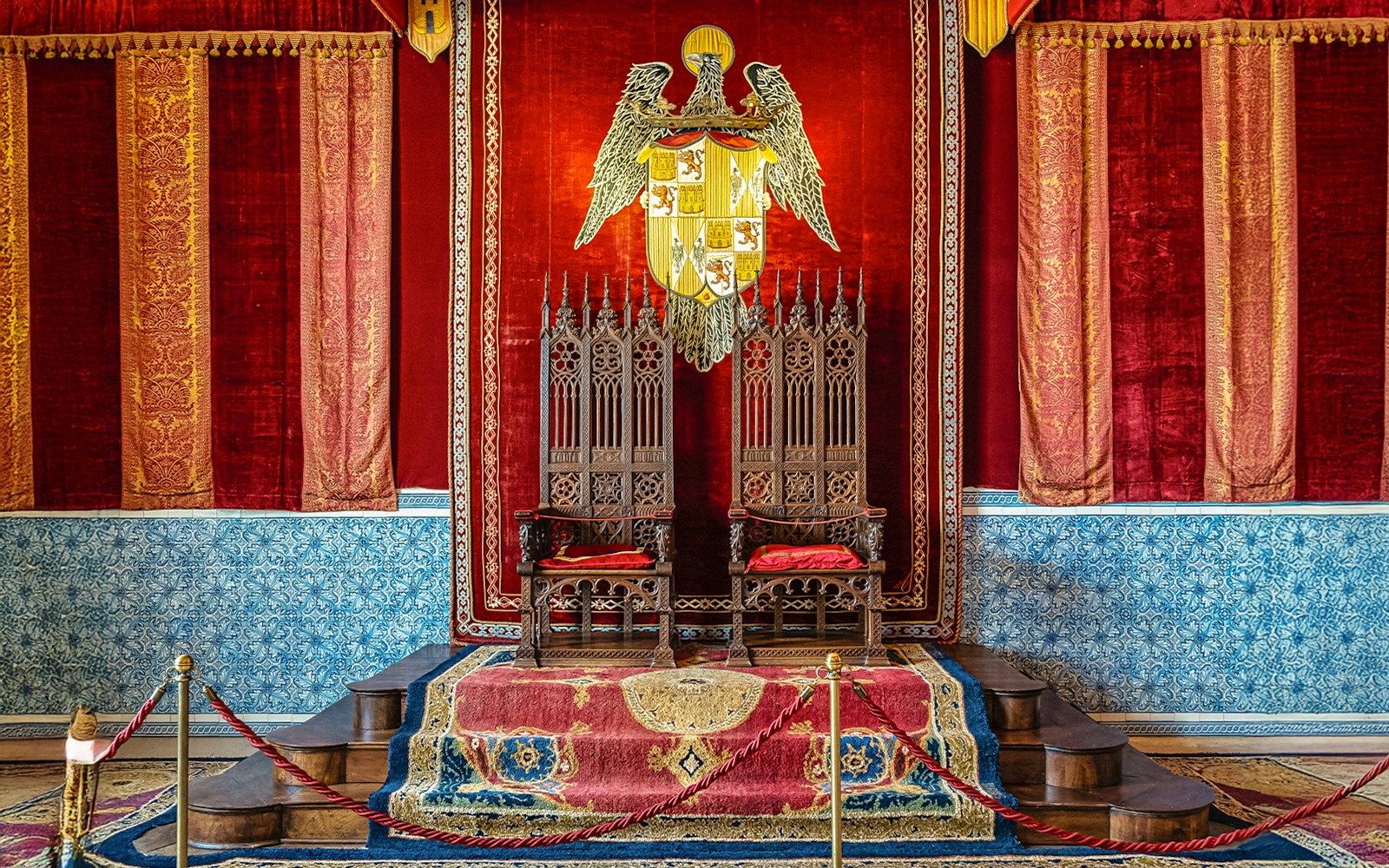 Throne Room in Alcazar Palace with ornate chairs and royal emblem.