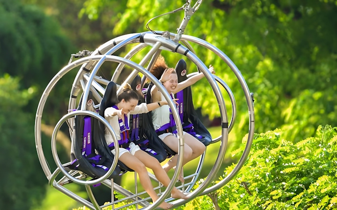 Two people enjoying the Slingshot ride in Singapore amidst lush greenery.