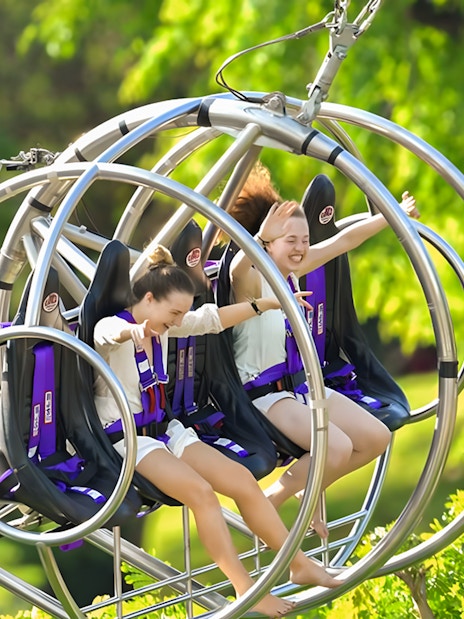 Two people enjoying the Slingshot ride in Singapore amidst lush greenery.