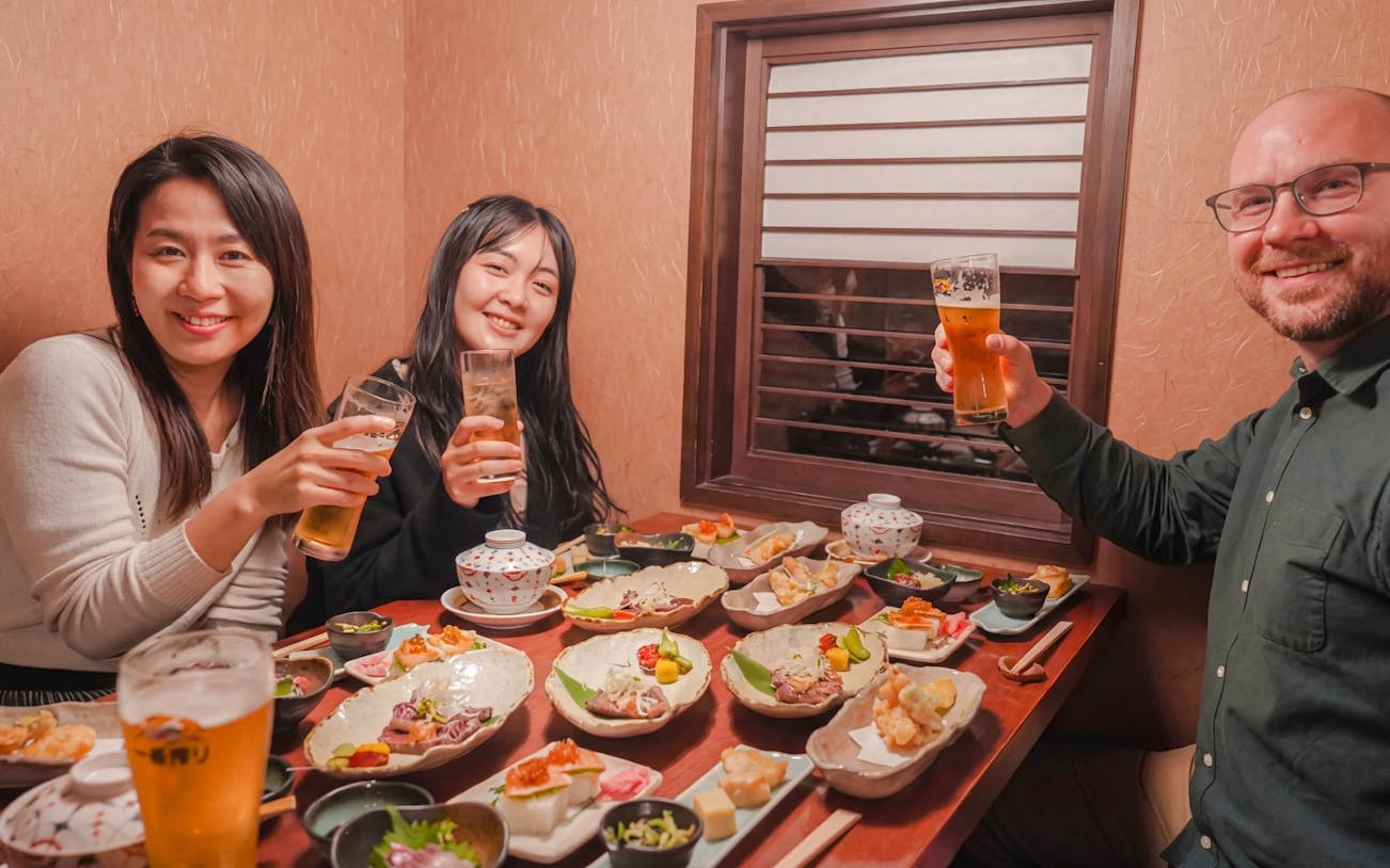Group enjoying traditional Japanese dishes and drinks on Kyoto Night Foodie Tour.
