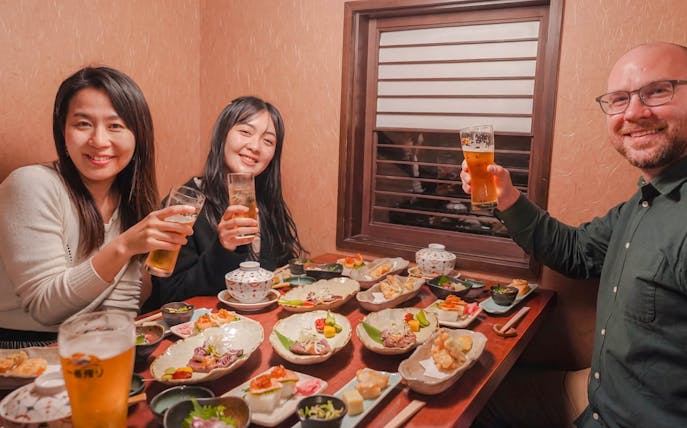 Group enjoying traditional Japanese dishes and drinks on Kyoto Night Foodie Tour.