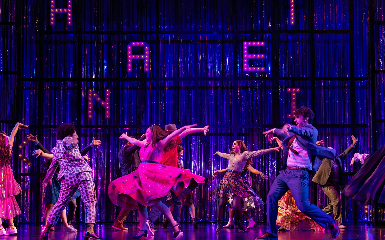 People dancing energetically on stage in Ohio, colorful outfits, vibrant backdrop.