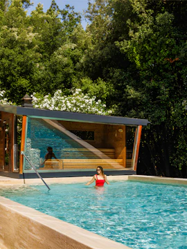 Woman enjoying outdoor pool at QC Termeroma spa surrounded by lush greenery.