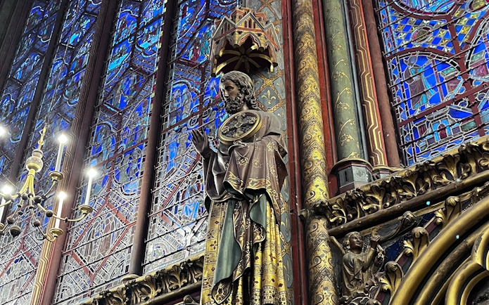Statue inside Sainte Chapelle with intricate stained glass backdrop, Paris.