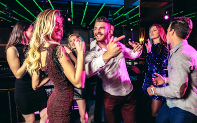 Young people dancing on a nightclub balcony with neon lights.