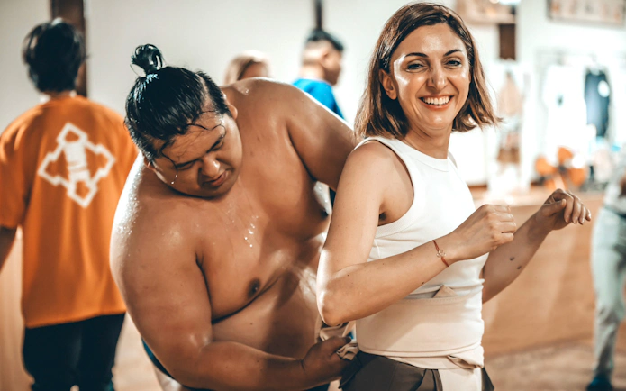 Sumo wrestler assisting woman with waist belt adjustment in Japan.