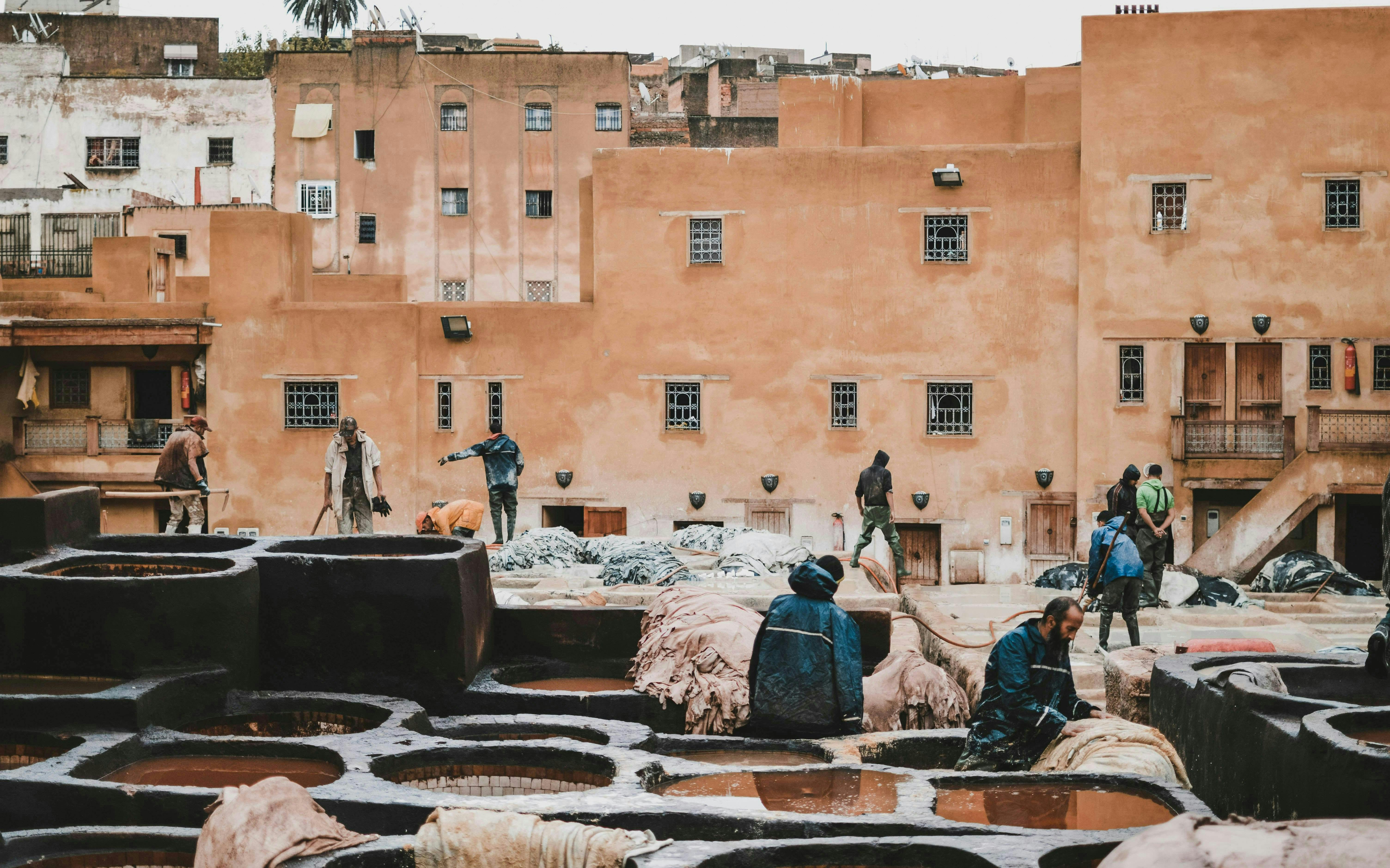 Workers at traditional tannery in Fes Old Medina, Morocco, surrounded by dyeing vats.