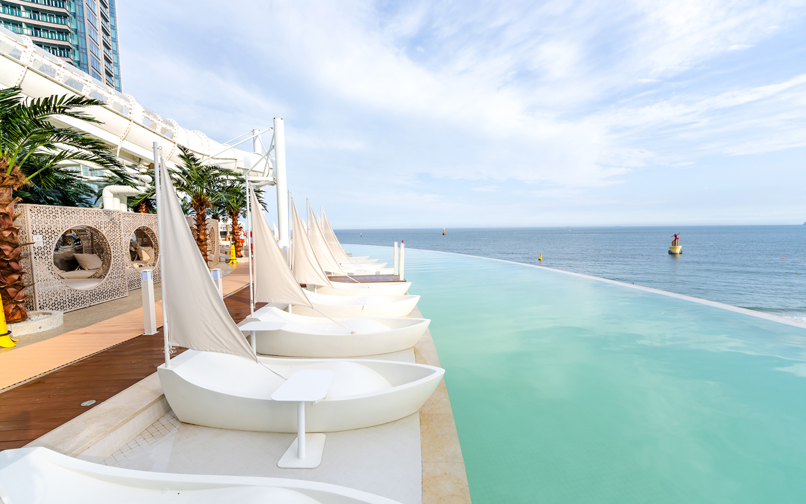 Boat-shaped sun loungers by Club D Oasis infinity pool with ocean view in Busan.