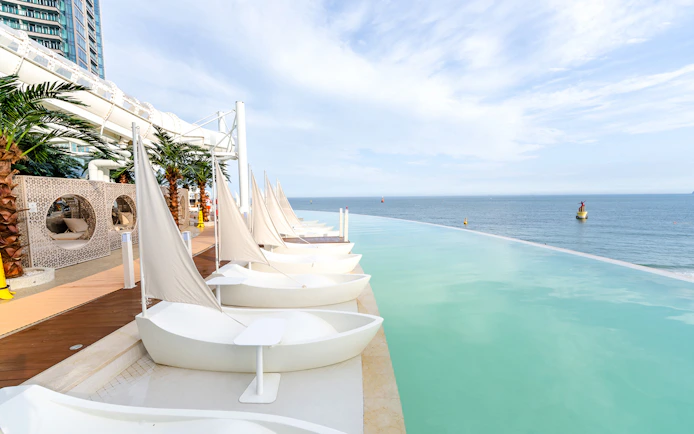 Boat-shaped sun loungers by Club D Oasis infinity pool with ocean view in Busan.