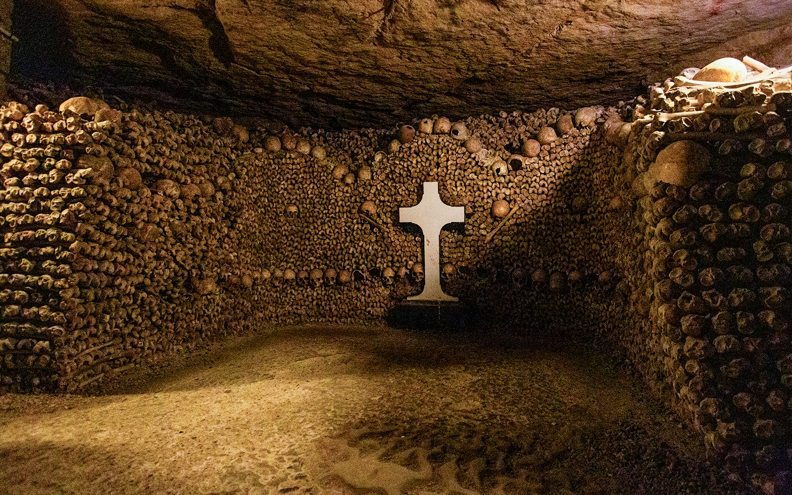 Tourists exploring Paris Catacombs, walking through tunnels lined with skulls and bones.
