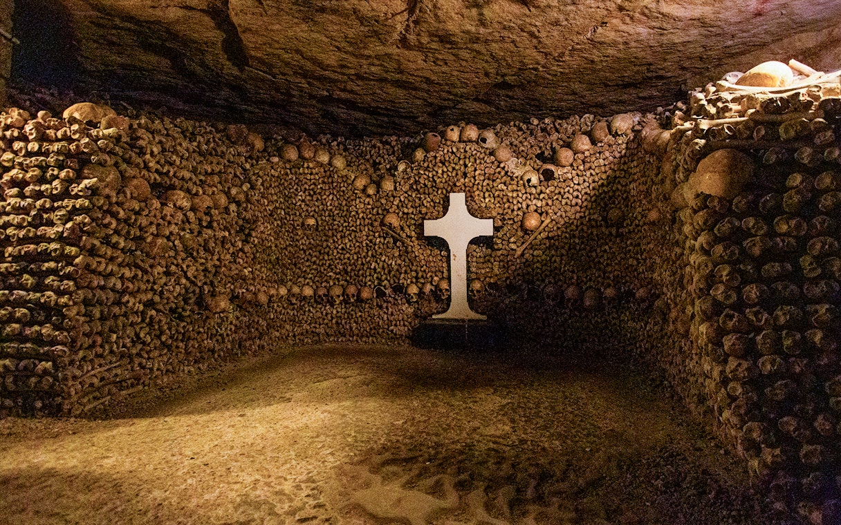 Tourists exploring Paris Catacombs, walking through tunnels lined with skulls and bones.