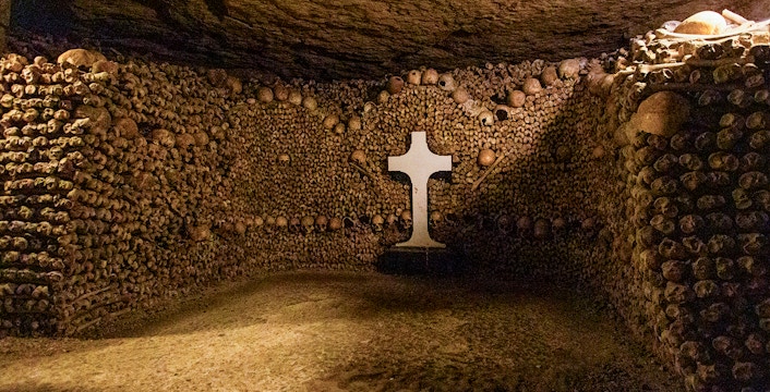 Tourists exploring Paris Catacombs, walking through tunnels lined with skulls and bones.