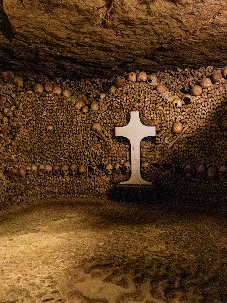 Tourists exploring Paris Catacombs, walking through tunnels lined with skulls and bones.