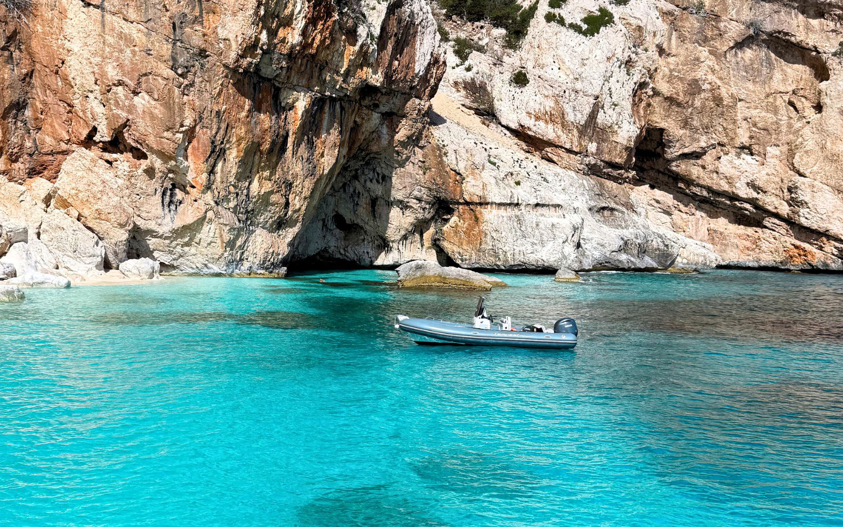 Dinghy in turquoise waters near rocky cliffs, Gulf of Orosei, Cala Gonone.